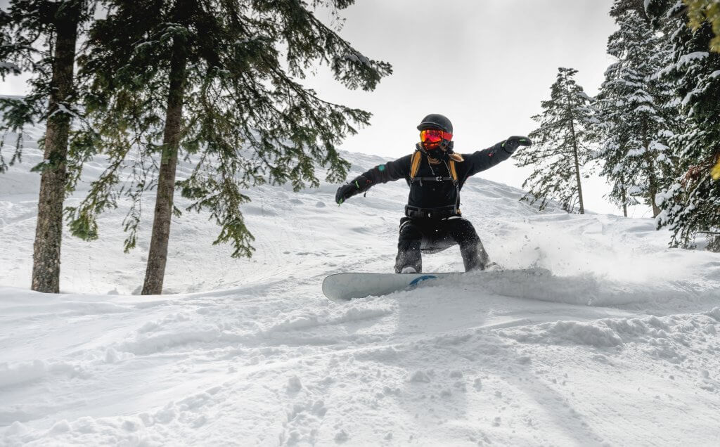 A woman on a snowboard in a helmet quickly descends from the ski slope, creating a plume of snow behind her